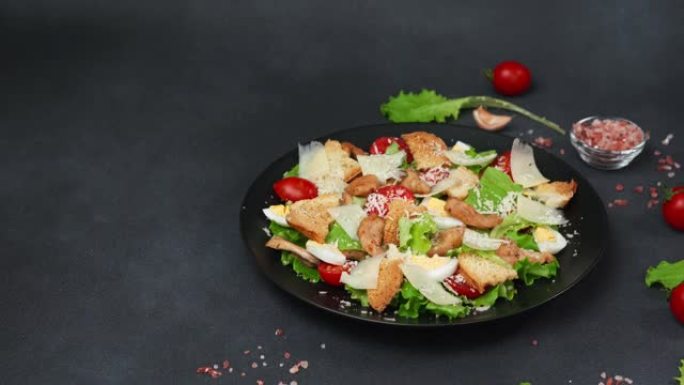 凯撒沙拉配鸡肉，生菜叶，樱桃番茄，磨碎的帕尔马干酪，在黑色背景下的黑色盘子中