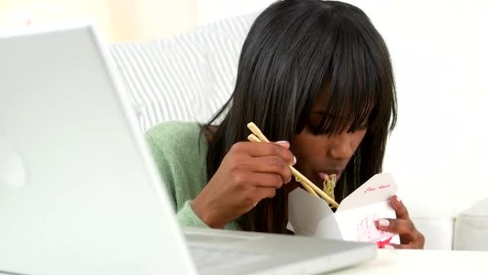 黑人妇女在使用笔记本电脑时吃中国外卖