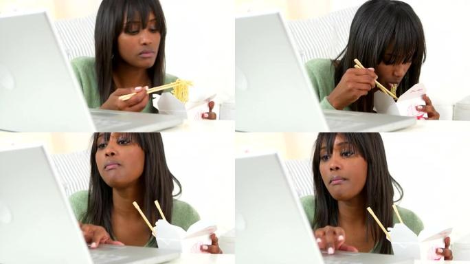 黑人妇女在使用笔记本电脑时吃中国外卖