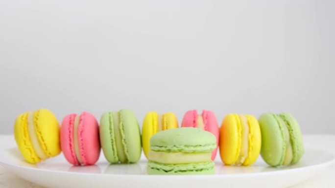 许多彩色的法国马卡龙甜点站在白色背景上的盘子上，一只手在一个圆圈中扭曲了一个绿色，为咖啡店做广告。