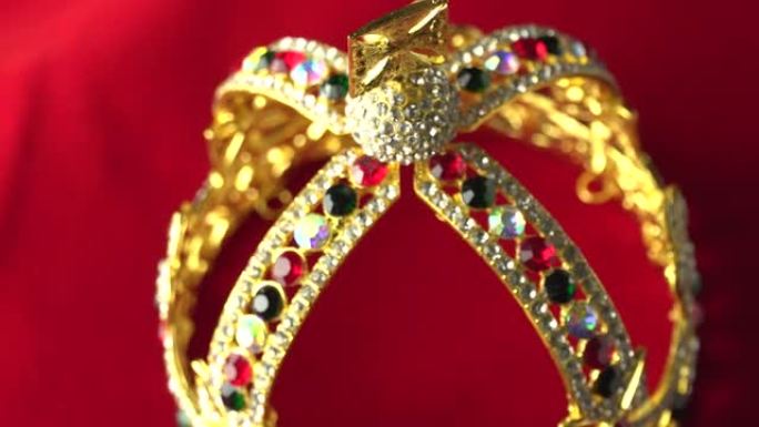 金色皇冠配豪华彩色珠宝和钻石。有反射和灯光火花。在红色皇家色表面上缓慢旋转。4k，uhd。专注于顶部