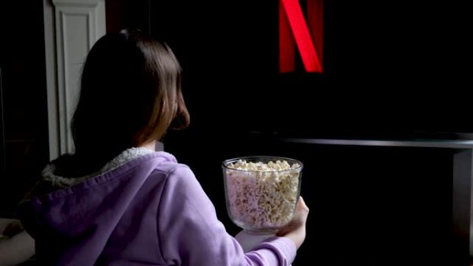 十几岁的女孩坐在地板上，在电视屏幕保护程序的大屏幕上观看netflix慢动作闪烁在年轻女子的手中，爆