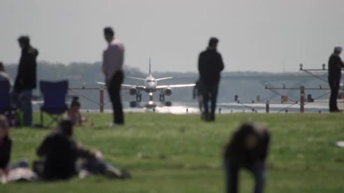 飞机从跑道上起飞，在前景的公园里的人