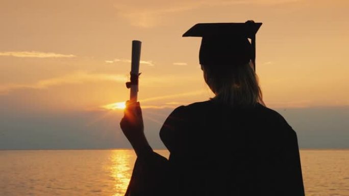 一个拥有学士学位的女人，在日落时穿着长袍和研究生帽