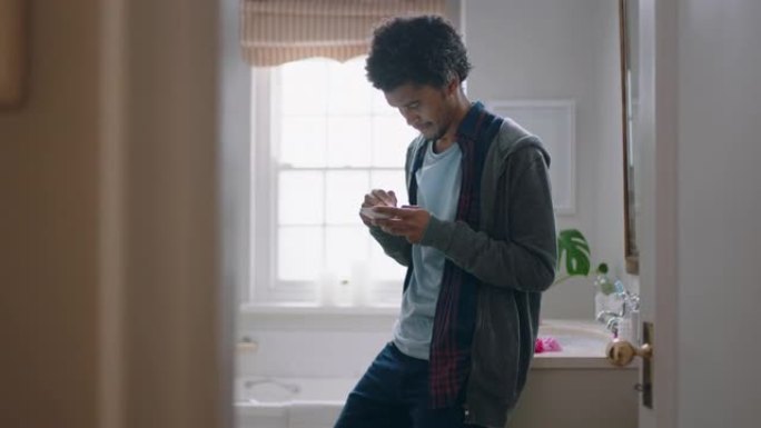 年轻的混血儿男子在浴室使用智能手机发短信，早上上班前在线浏览社交媒体信息
