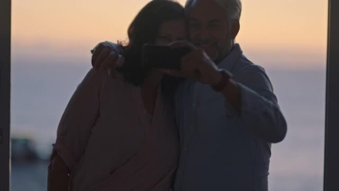 幸福的老夫妻在日落时使用智能手机拥抱在社交媒体上享受成功的退休分享假期