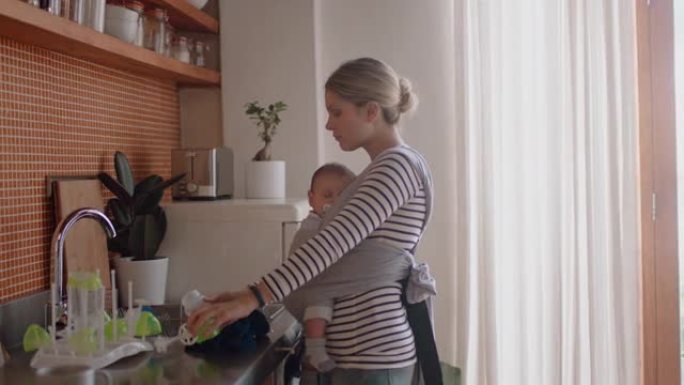 年轻的母亲抱着睡着的婴儿在家打扫厨房工作家务妈妈享受母亲的责任照顾孩子