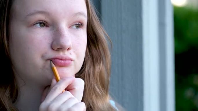 一个年轻的少女女孩手里拿着一支铅笔的悲伤沉思的集中脸认为把它放在她的嘴边的地方文本培训学校课程青春期