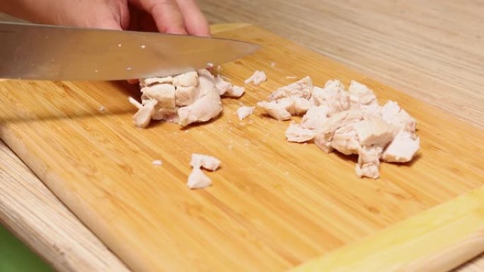 家庭主妇在家庭厨房的桌子上用钢刀将新鲜的chiken肉切成薄片。