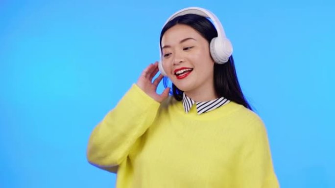 亚洲女人，耳机，听音乐，跳舞和娱乐在蓝色背景上。娱乐、广播和流媒体与模型空间，年轻的z世代女性在工作