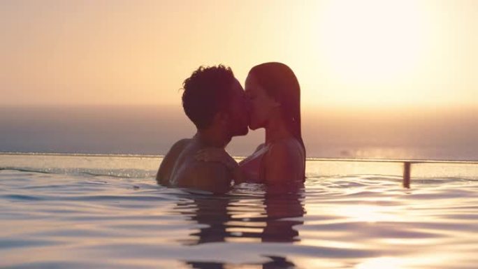 浪漫的情侣在游泳池接吻，享受豪华酒店的蜜月假期，日落时可以看到美丽的地中海海洋