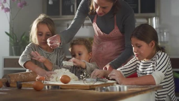 女人和她的孩子在厨房里一起烘烤的肖像。妈妈教她的小孩如何做饼干。兄弟姐妹帮助他们的母亲做饭。童年快乐