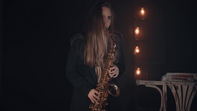 一个年轻女孩在黑色背景下的阴霾中在舞台上演奏萨克斯管。背景中有不活跃的照明