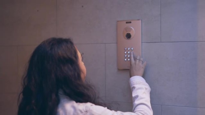 年轻的西班牙女孩按下安装在瓷砖内墙上的可视对讲数字键盘上的按钮。dolly-out