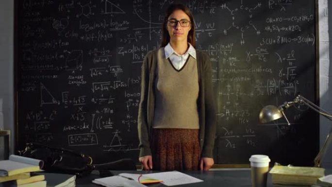 放大: 大学教室里年轻女教师的肖像站在黑板前，用数学公式。在大学图书馆学习的理科生看着相机微笑
