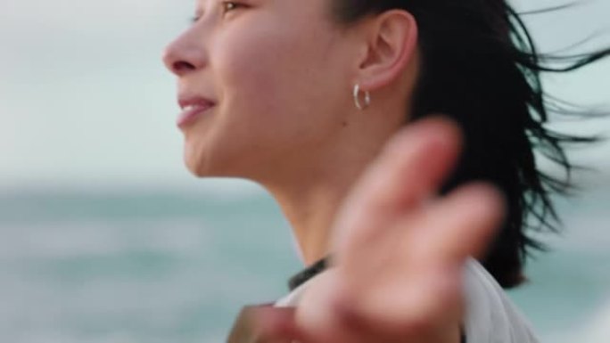 快乐的亚洲妇女享受自由的肖像，手臂举起，在日落的海滩上感受快乐，在风吹拂的头发中探索旅行