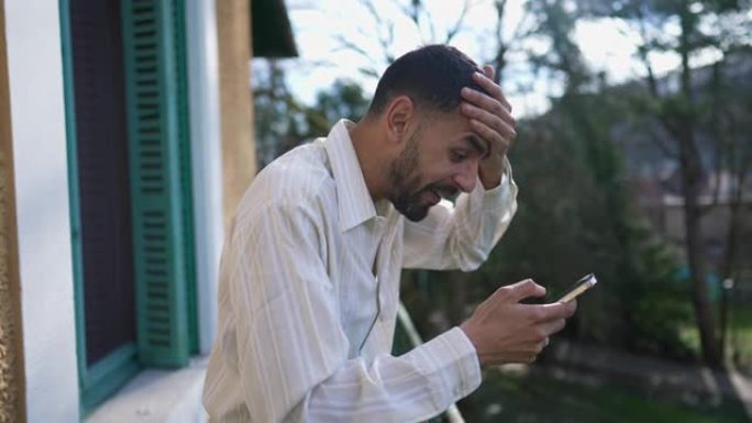 一个激动的阿拉伯年轻人在阳光明媚的日子里站在阳台上时，对手机设备上的正面信息做出了难以置信的反应