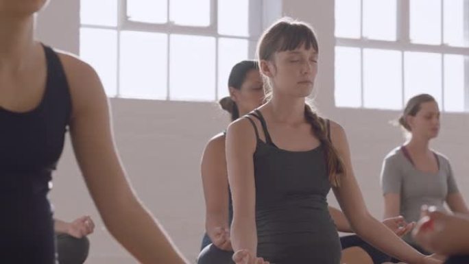 年轻怀孕的白人妇女在瑜伽课上练习莲花姿势享受团体冥想练习日出时在健身室放松