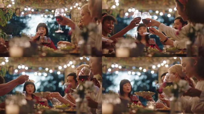 多种族朋友在晚宴上庆祝烤面包喝酒享受快乐的团圆聊天分享食物晚上坐在户外4k