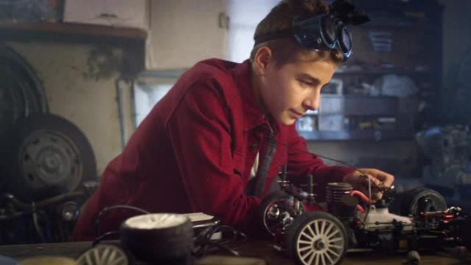 在为学校科学博览会建造功能玩具车的车间里，戴着护目镜的十几岁男孩的肖像。快乐的年轻机器人爱好者使用笔