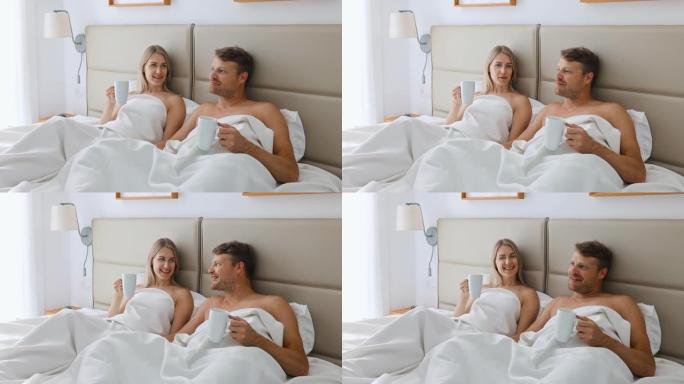 幸福的夫妇躺在床上，在家里的卧室里喝早间咖啡