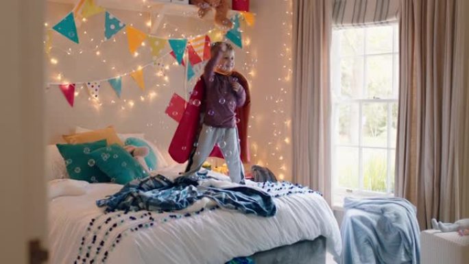快乐的小男孩跳上床上穿着戏服玩玩具枪射击泡泡游戏在家里五颜六色的卧室享受嬉戏的想象