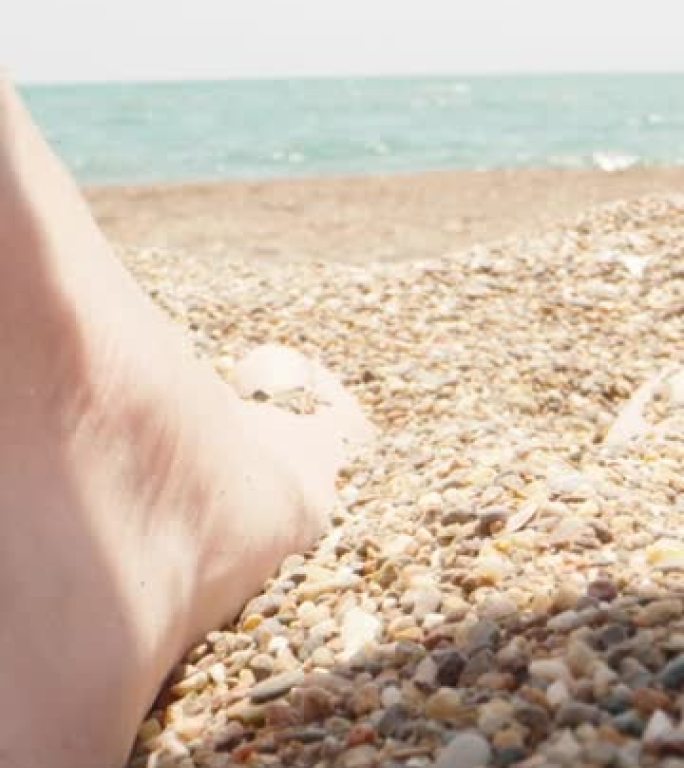 女人的脚踩在小海石上，特写。背景中的大海。垂直。社交媒体