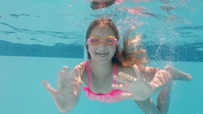 快乐的小女孩在游泳池水下游泳微笑挥手享受在水晶般清澈的水中游泳戴着护目镜享受夏天4k