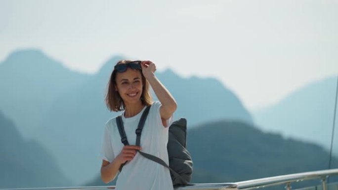 游客站在酒店的观景台上，背靠蓝色背景的山谷景观模型。穿着便服眼镜的时尚年轻女孩从山上欣赏景色。