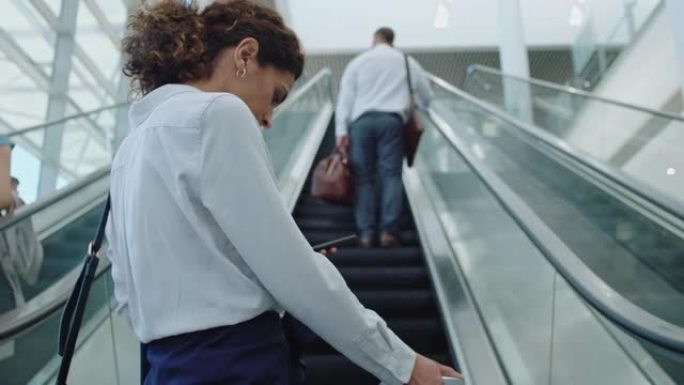 女商务旅行者走在机场，带着购物车走上自动扶梯，国际商务旅行的女行政人员查看智能手机4k上的信息