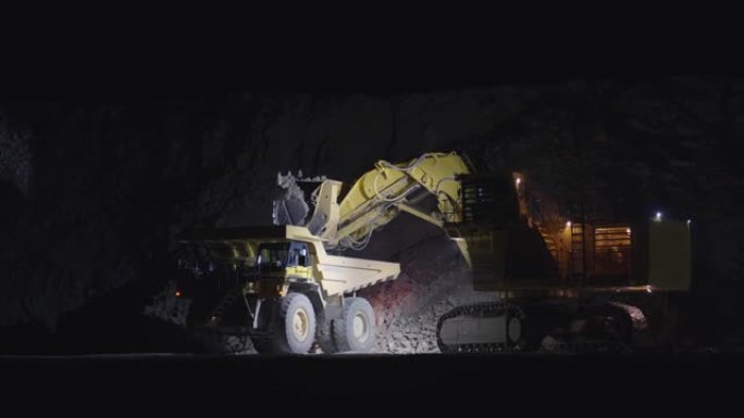大型escavator夜间在自卸车中装载矿石，慢动作