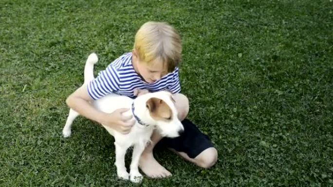 快乐的金发男孩和杰克罗素梗宠物狗在草坪上玩耍。
