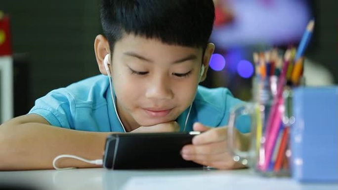 亚洲儿童在智能手机上使用带耳塞的数字平板电脑。