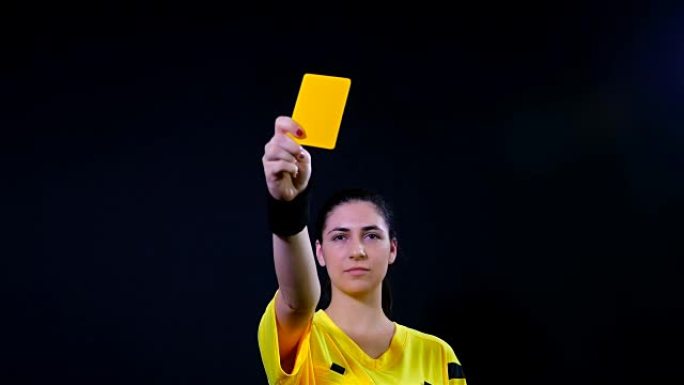 女子足球裁判在黑色背景上显示点球黄牌，4k