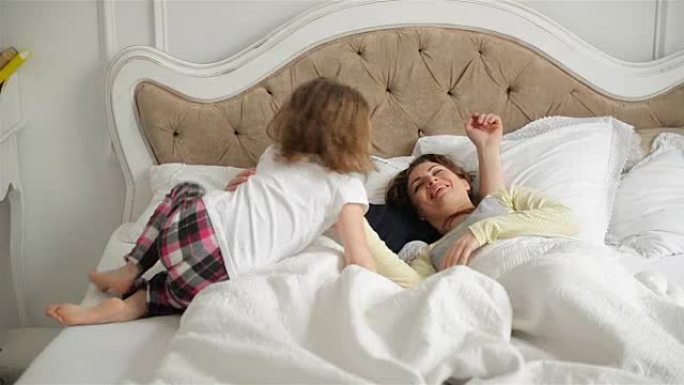 年轻夫妇一起睡在家里的床上。活跃的小女孩正在唤醒她熟睡的父母