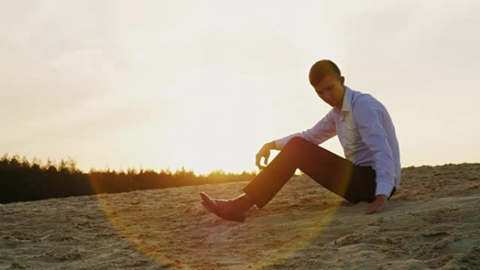 体贴的年轻商人坐在沙滩上，看着日落时从沙滩上爆发出来。概念: 时间的短暂，变化