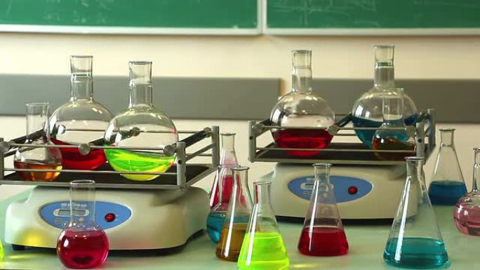 带有彩色解决方案的实验室玻璃器皿在两个振动台上同步旋转，一些烧瓶围绕