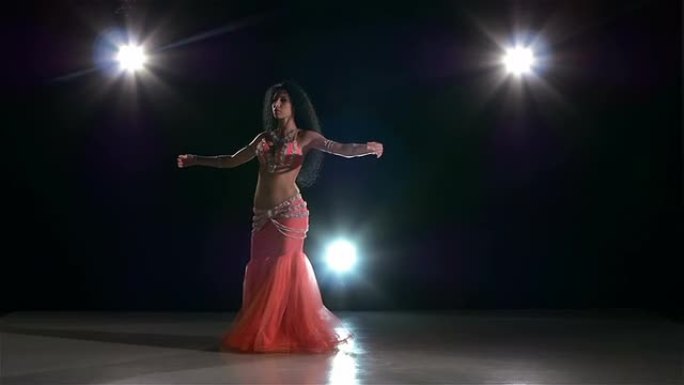 一位欧洲女肚皮舞演员开始在黑色，背光，慢动作上跳舞