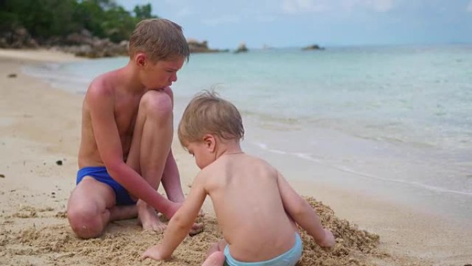 一个年轻人在海滩上和孩子玩耍。制作砂模