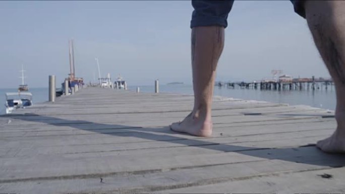 年轻人在码头上走向海洋。男孩在夏日走在木码头上。