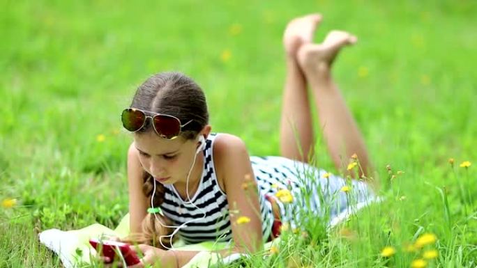 漂亮女孩躺在绿草地上，使用红色智能手机