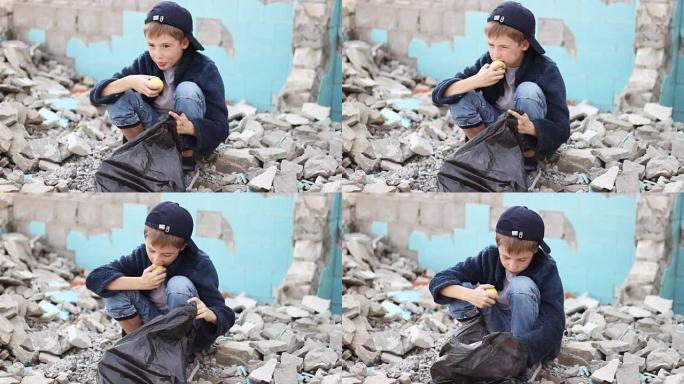 无家可归的孤儿男孩在房子的废墟中寻找包装中的食物并吃苹果