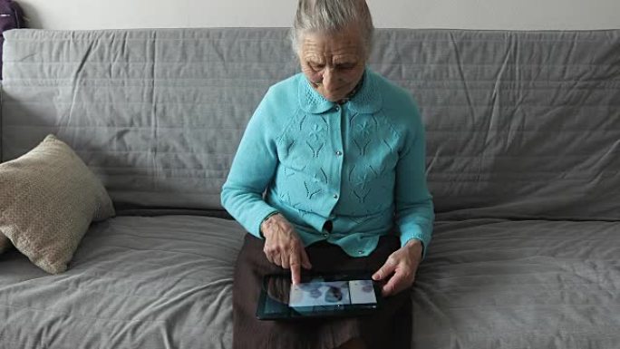 一位老妇人坐在沙发上，使用数字平板电脑。