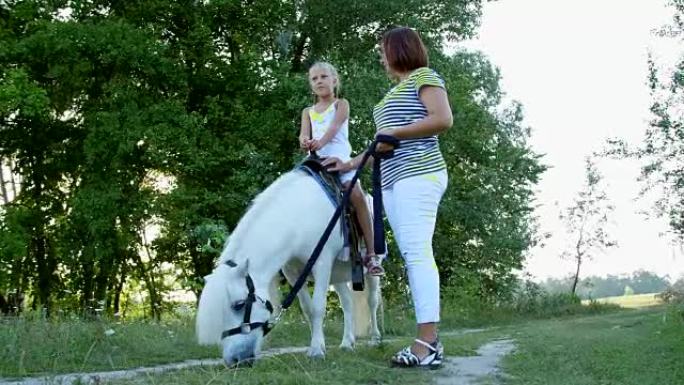 妈妈和女儿在田野里走来走去，女儿骑着小马，妈妈拿着小马当缰绳。快乐快乐的家庭假期。户外，夏季，森林附