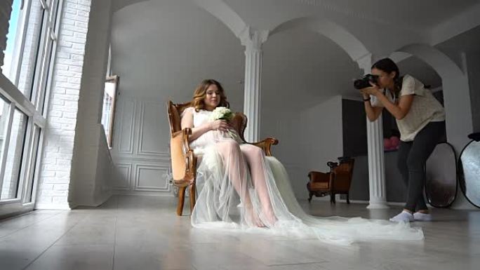 美丽的年轻孕妇坐在白色的椅子上，向摄影师摆姿势