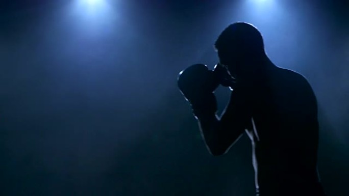 在剪影中可见的工作室中的年轻男运动员拳击