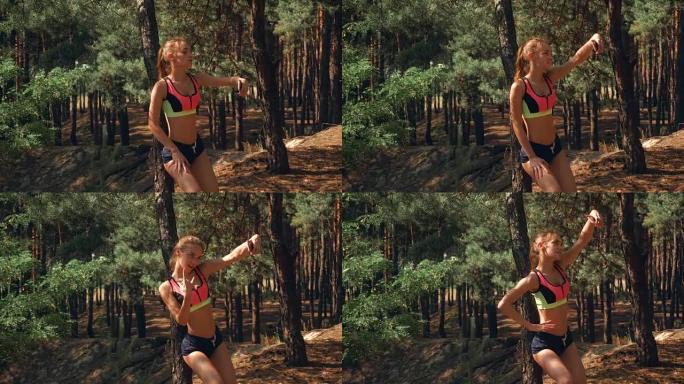 腹部有弹性的运动女孩站在树林里，看着你的手机