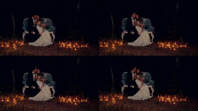 新婚夫妇晚上坐在黑暗森林中的沙发上拥抱和亲吻。