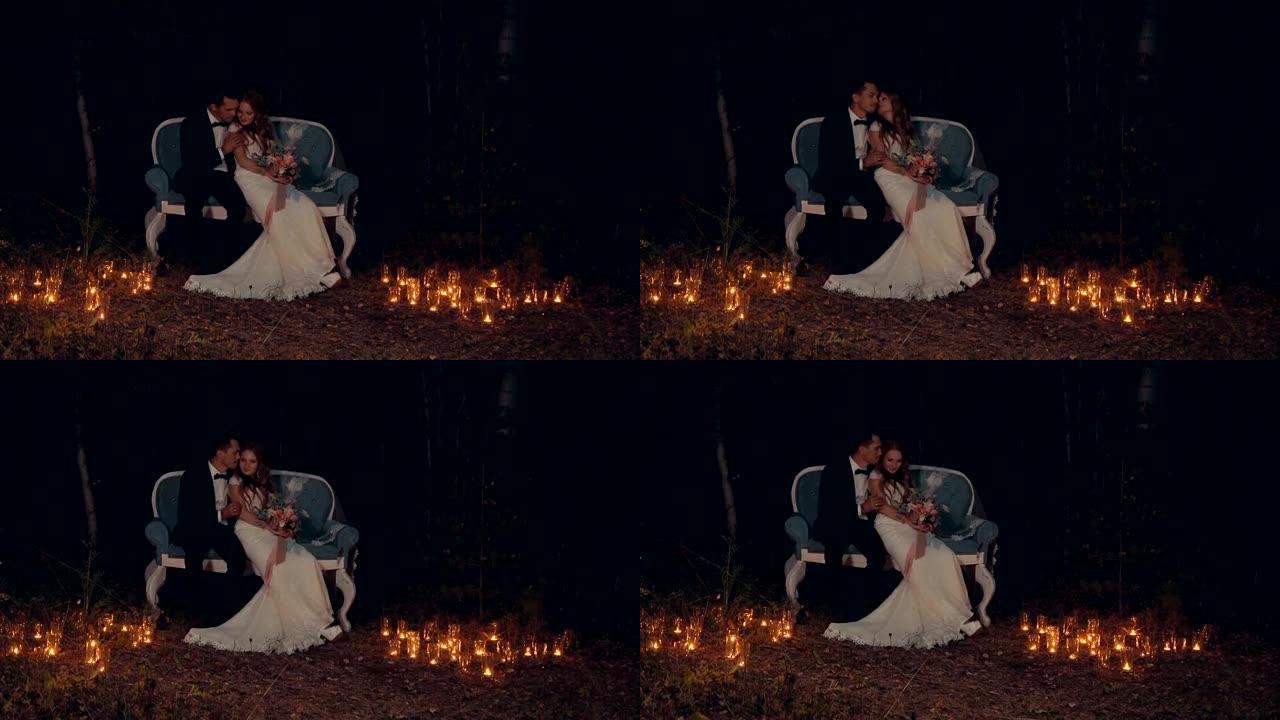 新婚夫妇晚上坐在黑暗森林中的沙发上拥抱和亲吻。