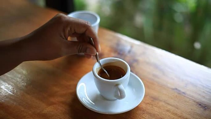 女人拿勺子，在一杯咖啡里搅拌咖啡。